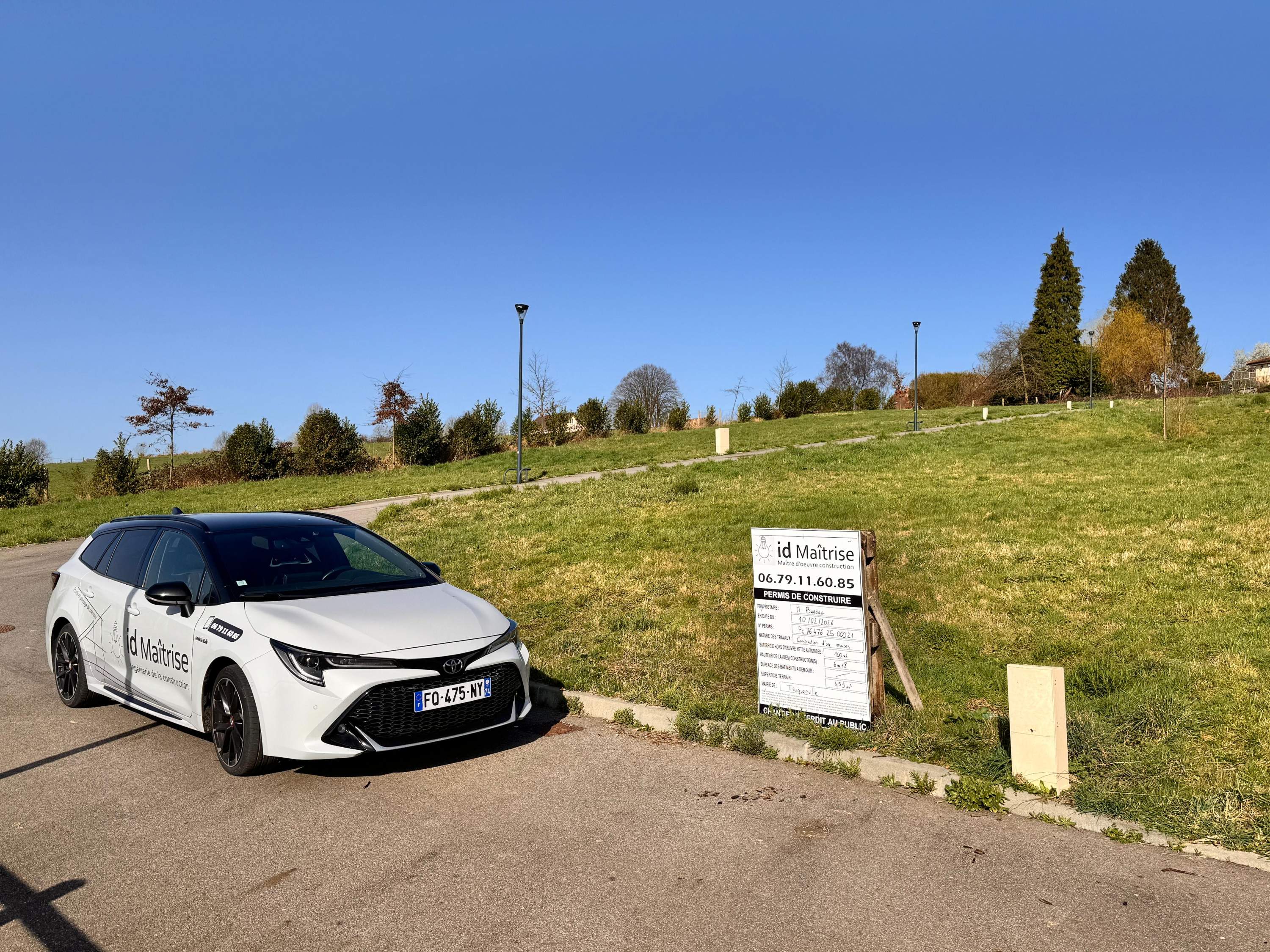 Panneau réglementaire de permis de construire planté en bordure de terrain, avec une maison en construction à l'arrière-plan